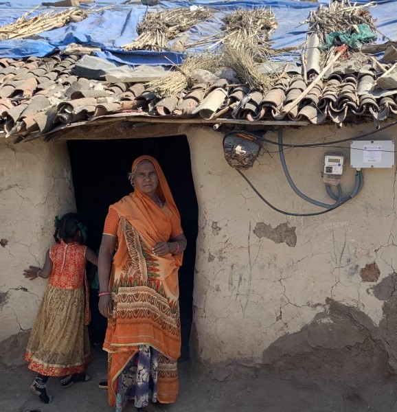 Women in orange sarong standing outside home with electricity mounted on outside wall