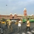 People walking in busy intersection with large with green streetcar and large red brick building in the background